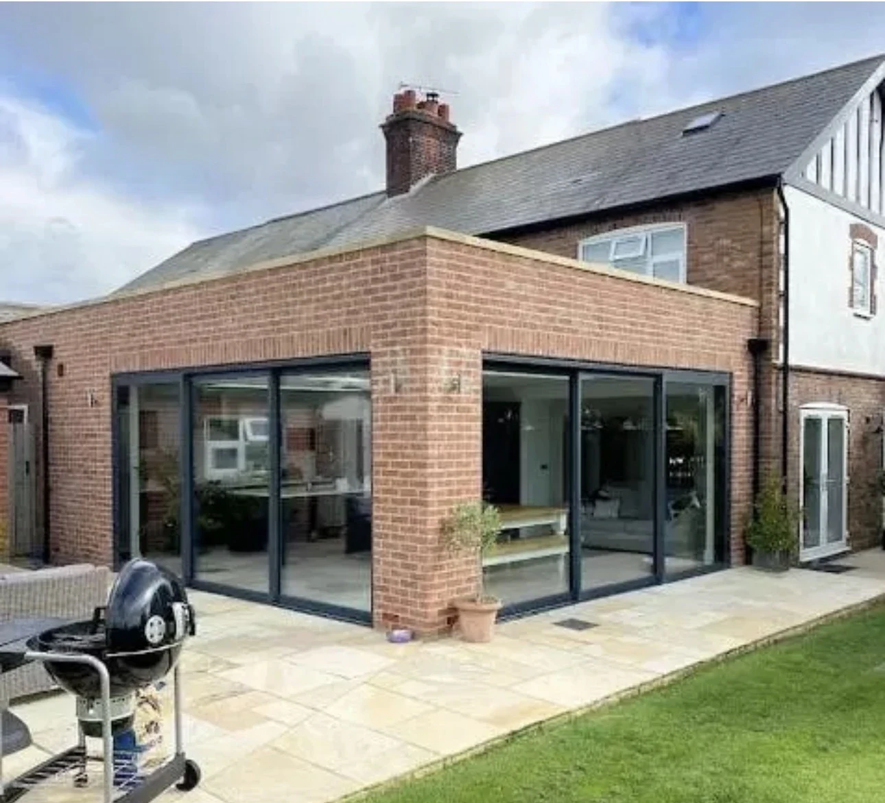 Brick extension opening onto a paved terrace through dark-framed glazed doors