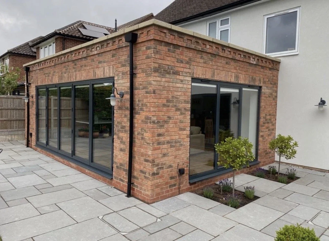 Brick extension beside light paving with dark-framed glazed doors